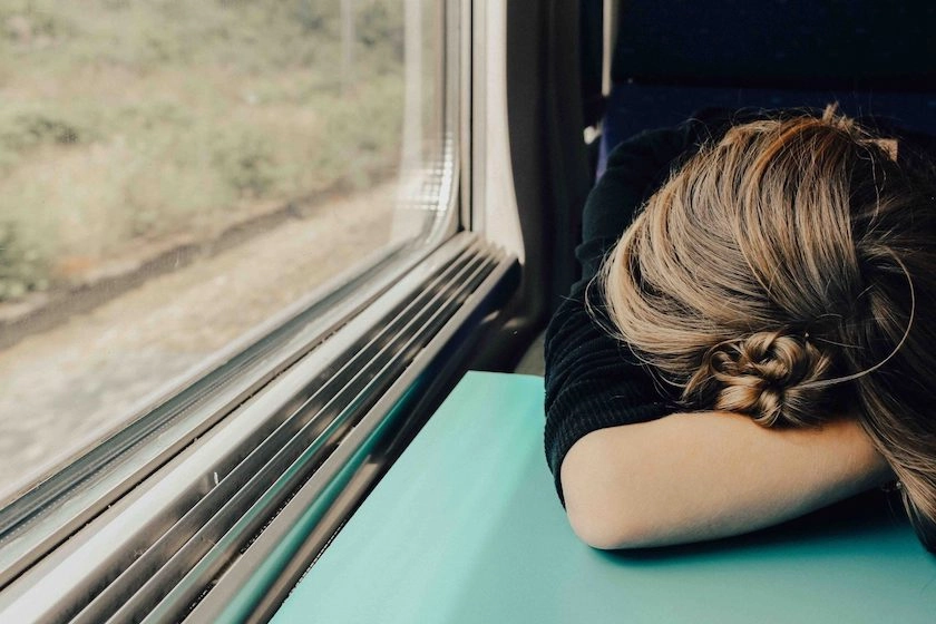A woman on a train or bus puts her head down in her arms.